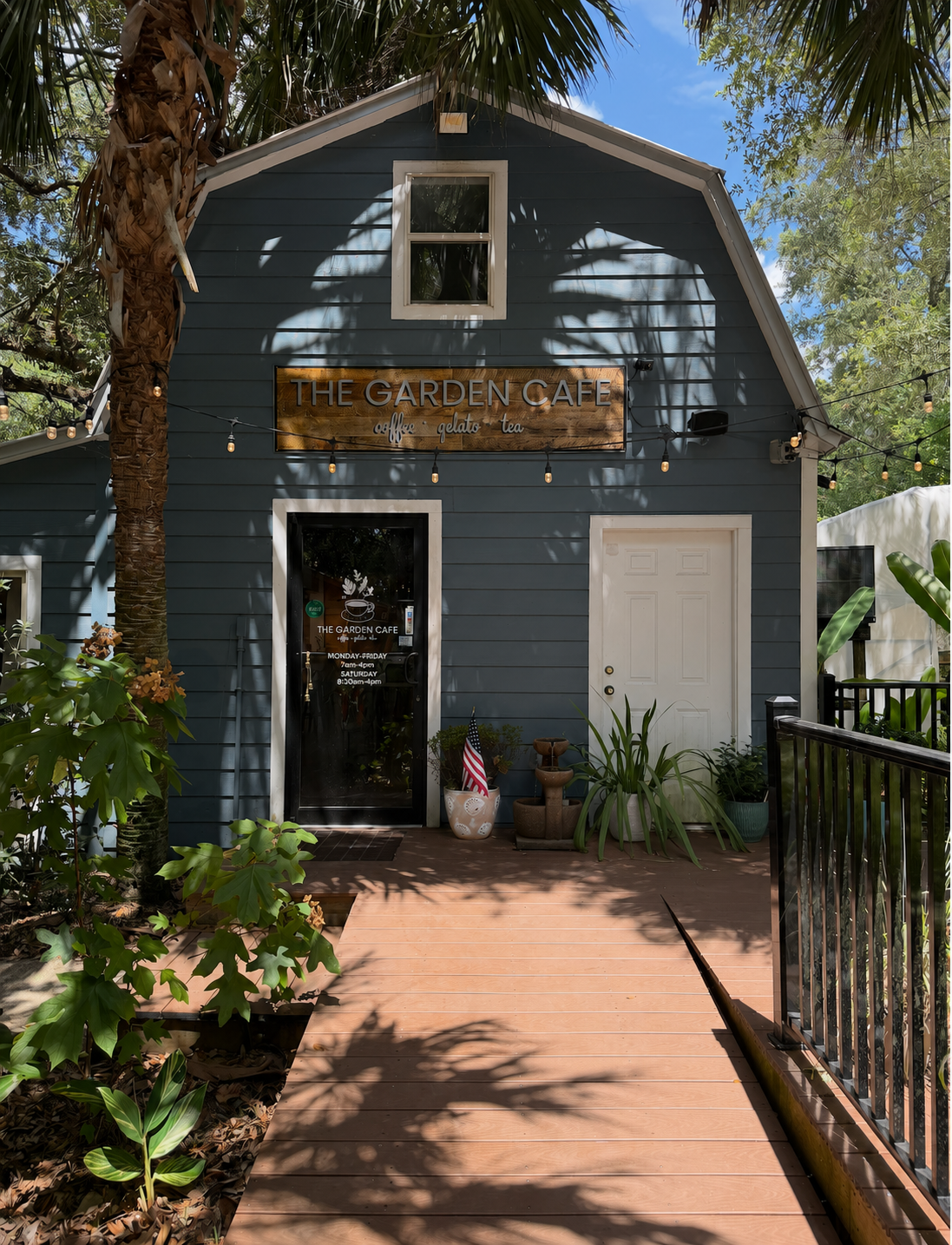 The Garden Cafe exterior at Pinelands Nursery — a small blue building surrounded by palms and garden plants